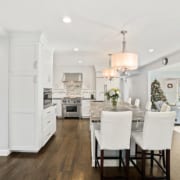 A kitchen with dark wood floors, white cabinets, simple and clean stainless steel finishes. The large island has white full-back seating for 6, and a black with white swirls marble counter-top.